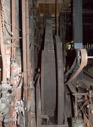Belt beside the flywheel which drives the main shaft of the machine shop. Note that here they had one common engine that drove a common shaft that in turn drove the various machines by way of another belt drive.