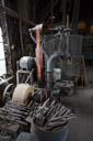 Background is a drill press with modern electric motor replacing the belt drive. In the foreground is a whetstone with many bits in place ready for sharpening.