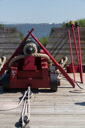Typical cannon setup. The timbers crossed over the canon are 'handspikes' used to handle the cannon mainly when aiming the cannon in conjunction with the elevating guoin. 

To the To the side and leaning against the wall are the wormer, sponge and rammer.

The various block and tackle are used to pull the cannon back into position to be charged and back forward into firing position.