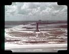 Aerial view of the Saturn V launch complex with pad 39A in the center. The sphere to the right is the liquid oxygen storage tank, liquid hydrogen storage tank is in the foreground, mobile service structure is parked in the left center just off the crawler way and the vertical assembly building is in the back ground with two parked mobile launcher.