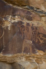 Dinwoody creature. Arms with elbows indicated and four fingers on each hand. Legs indicated but no knees. Torso is fully pecked. No neck is indicated and head? is stylized with elaborate head dress.  Dinwoody on right arm appears to have been created at the same time as the main character.  Also the outline figure to the immediate left of the main character and alot the stick figure? to the outline figure's immediate left. Note the single foot with toes indicated on the stick figure. The stick figure has a head treatment indicated, two arms and fingers indicated. The figure to the extreme right of the photograph appears to be more recent or may have been re-pecked more recently. The less distinct figures to the lower left of th photograph appear to be one sort of fremont character and maybe a zoomorph.  Between the legs of the main character, is there an indication of a baby being born?? Are the indistinct characters at the lower left artifacts of the shamen talking and working out among themselves what to render as a main figure.  All these petroglyphs are clearly visible from a distance and were suitable for use a part of a ceremony with audience participation.